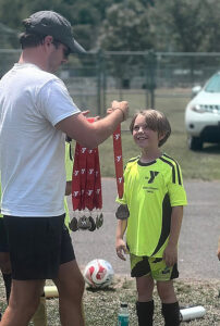 Man presenting a medal to a child at an athletic event.