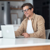 A male student sits at a white counter with his laptop in front of him.