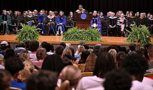 A woman on stage presenting to a theater full of students.