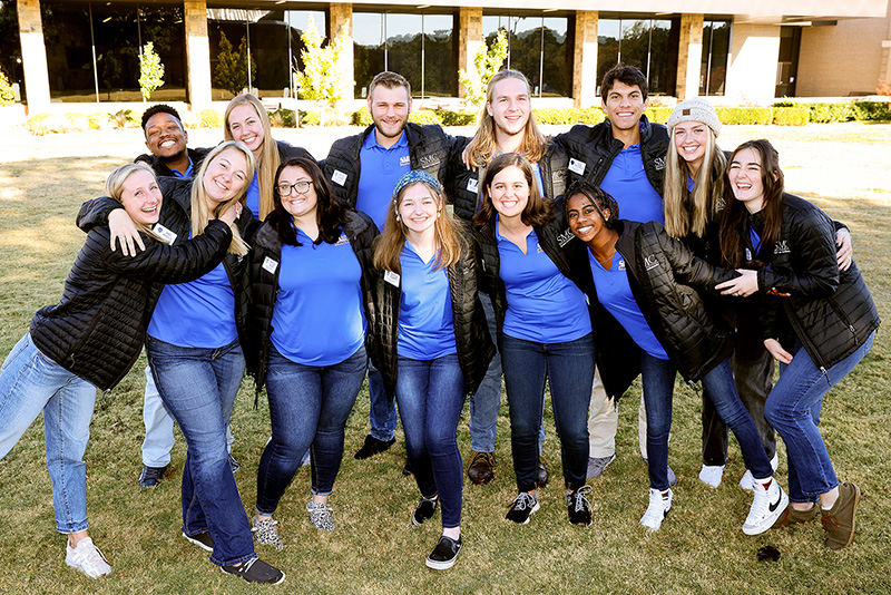 Four male and nine female SMC students pose together on a lawn in two rows.