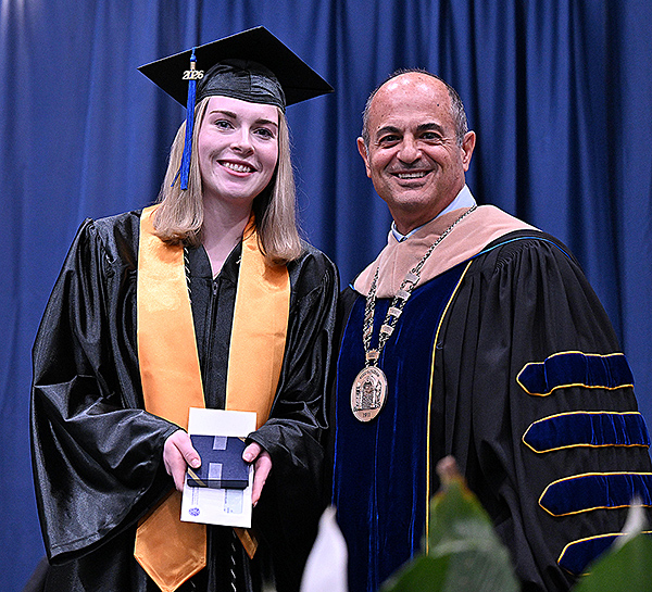 Young woman receiving award from man in graduation regalia.