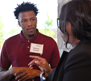 An African American student wearing a nametag speaks with a recruiter at a campus networking event.