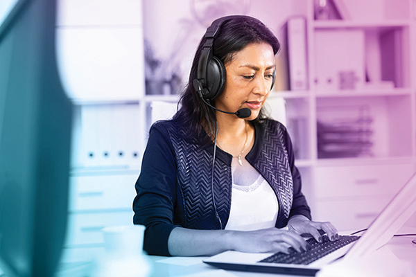 A woman with headphones at a computer in an office setting.